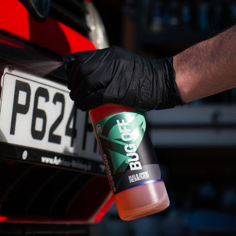 A bottle of Bug Off bug and grime remover being squirted on a red car