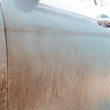 Close-up of a dirty metallic grey car door panel covered in dust and grime, with a chrome door handle visible on the right.