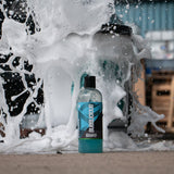 A bottle of Bubblicious car shampoo in front of a bucket of bubbly water